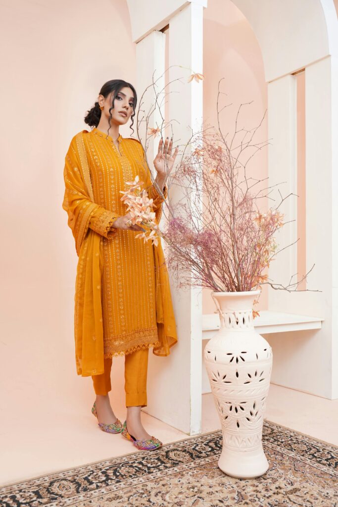 Stylish young woman modeling traditional Pakistani clothing indoors by a vase with dried flowers, representing trendy women’s wear in Kochi.