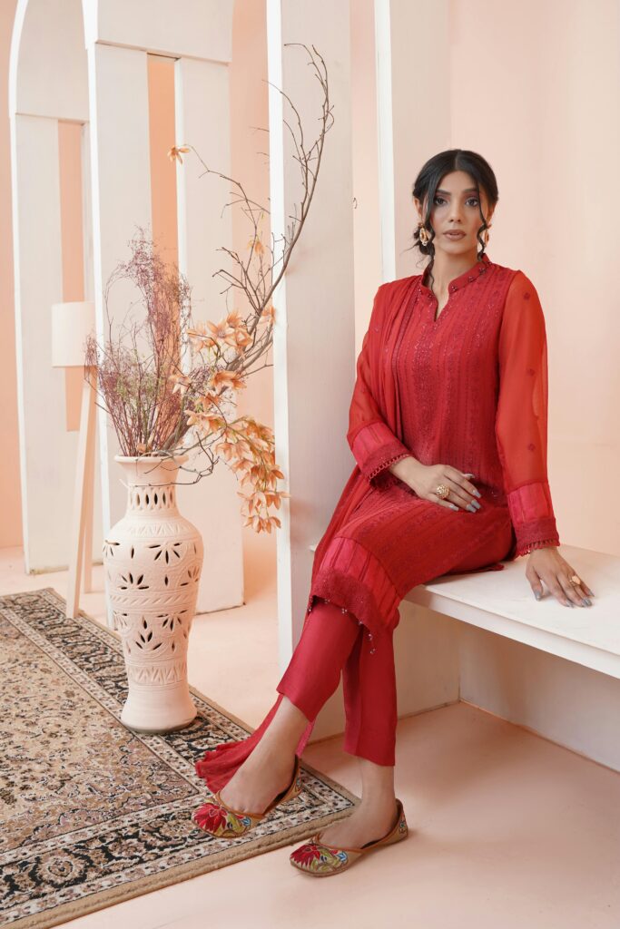 A woman in traditional red clothing sits elegantly indoors, showcasing Pakistani fashion and reflecting the grace found in plus-size-womens-clothing-in-Kochi.