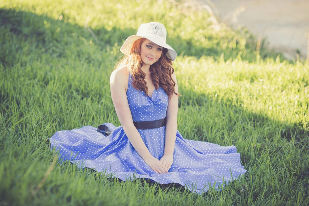 A young woman in a polka dot dress and sun hat sits on a grassy field, enjoying a sunny day — her look effortlessly blending modern charm with the elegance of a dhoti kurti.