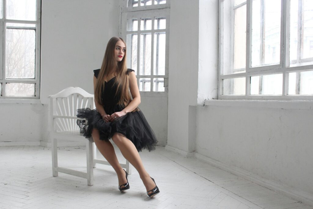 "A young woman in an elegant black dress poses in a bright room with large windows, showcasing beauty and style inspired by women’s western wear Kochi loves."